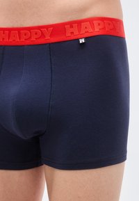 Μπλε σκούρα ανδρικά κοντά εσώρουχα με κόκκινη ελαστική ζώνη μέσης που φέρει τη λέξη «HAPPY» σε ανάγλυφα γράμματα. Λείο ύφασμα με ραφές λεπτομέρειες.