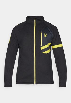 Zwarte zip-up jas van gestructureerde stof. Bevat gele accenten, een met rits afgesloten borstzak en een geborduurd logo aan de voorkant.