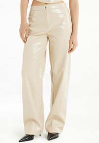Beige, glanzende, faux leren broek met wijde pijpen, een gestructureerd krokodillenpatroon, voorzakken en een knoopsluiting bij de taille.