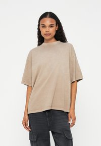 Beige oversized t-shirt med rund halsudskæring og korte ærmer, lavet af et blødt materiale, med en afslappet pasform og minimale sømdetaljer.