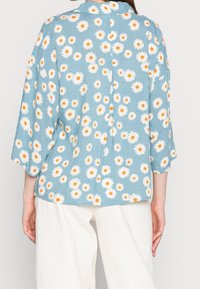 Blusa blu con un motivo floreale bianco e arancione, caratterizzata da una vestibilità comoda, maniche a tre quarti e tessuto texturizzato.