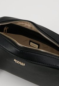Schwarze Handtasche mit Reißverschluss, strukturiertem Äußeren, goldfarbener Hardware und beigem Innenfutter. Verfügt über ein kleines Logoschild im Inneren.