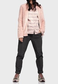 Puszysty różowy kardigan na jasnej w paski bluzce, w połączeniu z ciemnymi zwężanymi spodniami i wielokolorowymi trampkami. Widziane miękkie tekstury i suwaki.