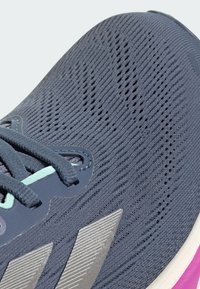 Sneaker met een donkerblauwe gebreide bovenkant, grijze accenten en mintgroene veters. Heeft een gestructureerde zool met roze highlights en zilveren branding.