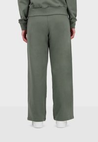 Pantaloni della tuta verdi, a vita alta e con una vestibilità comoda. Tessuto morbido, gambe ampie e cintura elastica; abbinati a sneakers bianche.
