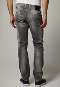 Grå denimjeans med slim fit, femfickorsdesign, synlig sömnad och varumärkesdetalj på bakfickan. Bärs med blå sneakers.