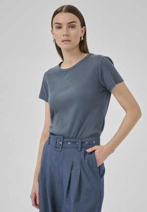 Blue ribbed t-shirt with short sleeves and a round neckline featuring an embroidered design. Paired with high-waisted striped trousers and a belt.