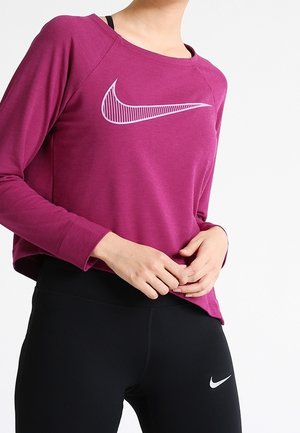 Langärmliges lila Sportoberteil mit einem weißen Nike-Logo, kombiniert mit schwarzen Leggings, die ein kleines weißes Nike-Logo aufweisen.