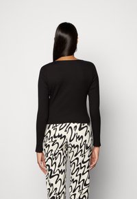 Musta ribatut pitkähihaine paita neliön muotoisella kaula-aukolla, yhdistettynä korkeavyötäröisiin housuihin, joissa on musta abstrakti kuvio valkoisella taustalla.