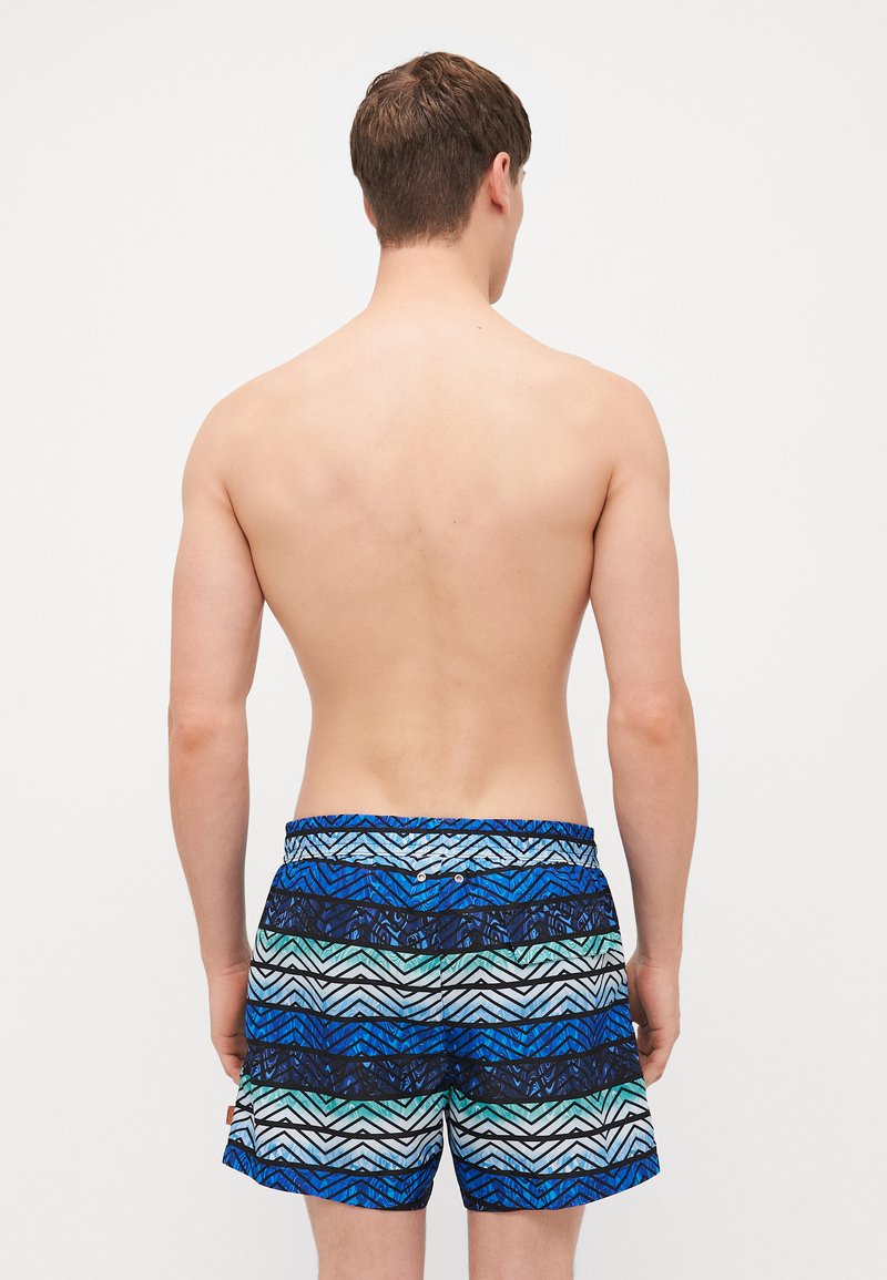 Badehose mit einem blauen und grünen geometrischen Muster und schwarzen Akzenten. Das Material scheint leicht zu sein; sie verfügt über einen elastischen Bund mit Knöpfen.