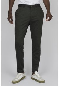Pantalones ajustados de un verde oscuro con una textura suave, que presentan un frente plano, presillas para el cinturón y un cierre de un solo botón, combinados con zapatillas blancas.