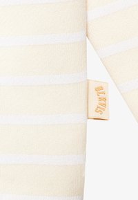 Csíkos kötött ruhadarab krém és fehér színben, texturált anyaggal és egy kis címkével, amelyen aranybetűkkel szerepel a "BLVCK" felirat.