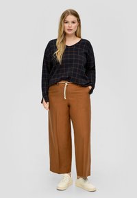 Suéter de cuadros azul marino con mangas largas y escote en V, combinado con pantalones sueltos de cintura alta marrones y zapatillas beiges.