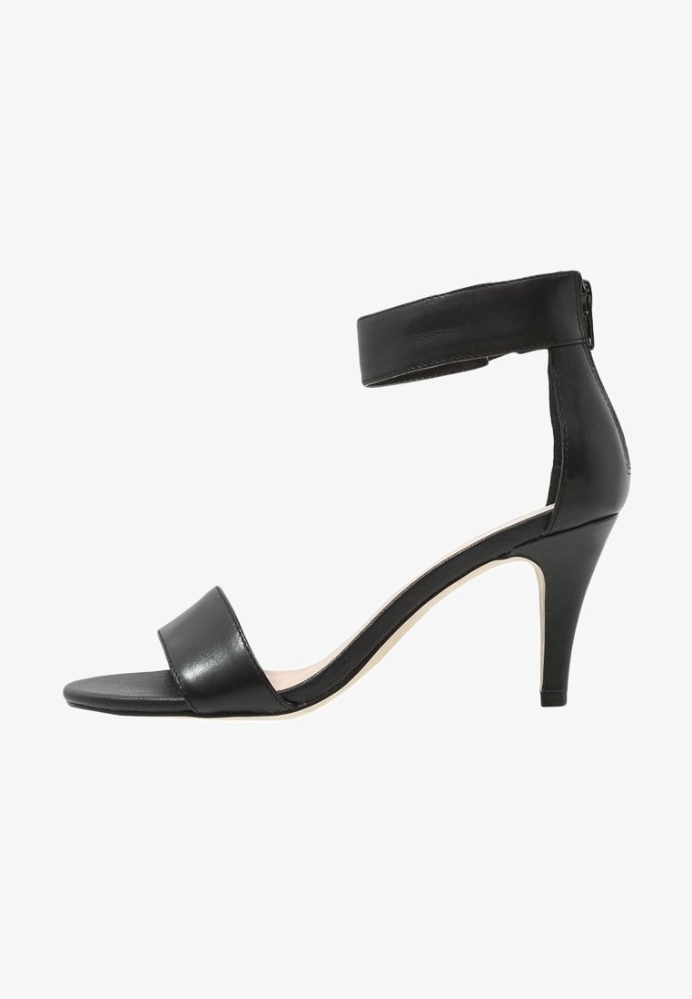 Sandales à talons hauts en cuir noir avec une bride de cheville, bout ouvert et un design épuré. La hauteur du talon est modérée, avec une finition lisse.