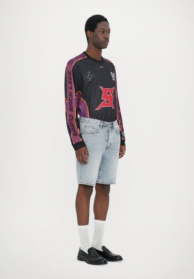 Tricou negru cu mânecă lungă, cu accente purpurii, prezentând imprimeuri grafice și textul „ADU ÎNAPOI VIAȚA”. Șorturi din denim albastru deschis și mocasini negri.