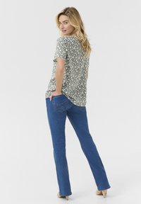 Top corto a maniche corte con stampa floreale verde e fiori bianchi, abbinato a jeans in denim blu con tasche posteriori e taglio dritto.