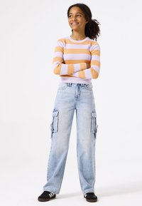 Top de manga larga a rayas en naranja pastel y lavanda, combinado con pantalones cargo azul claro que tienen bolsillos laterales y un ajuste relajado.