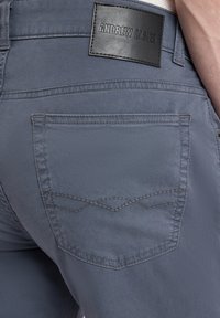 Graue Baumwollhosen mit einem Lederlabel am Bund. Die Gesäßtasche zeigt ein einzigartiges Nähmuster. Weiche Textur und schlankes Design.