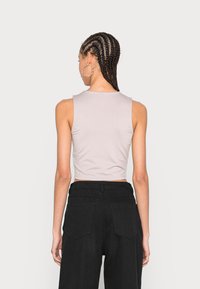 Top cropped cinza claro com decote arredondado e design sem mangas, combinado com calças pretas de cintura alta, exibindo detalhes nas costas.