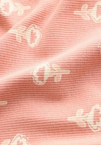 Weiches, geripptes Material in zartem Rosa, mit einem dezenten weißen Blütenmuster, das runde Formen und filigrane Details aufweist.