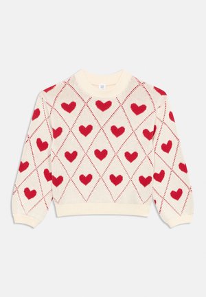 Adīta džemperis ar krēmkrāsas pamatni un sarkanu sirsniņu dimanta rakstu. Apaļa kakla izgriezuma, garām piedurknēm un ribotām aprocēm un apakšmalu.