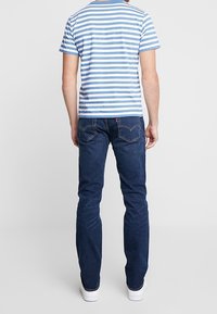 Randig blå och vit t-shirt i kombination med mörkblå jeans; har raka ben och minimalistiska vita sneakers.