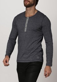 Pitkähihaisen tummansinisen paidan tekstuuri on miellyttävä, ja siinä on pyöreä kaula-aukko sekä viiden napin napitus keskellä.