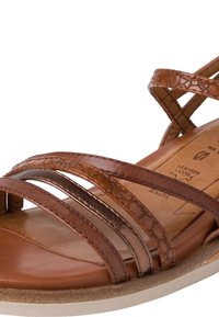 Sandales en cuir marron avec des brides superposées texturées et lisses, une semelle intérieure rembourrée et une semelle blanche visible sur le bord.