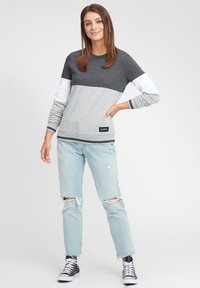 Felpa color blocco grigia e bianca con maniche lunghe, polsini a costine e un'etichetta nera. Indossata con jeans strappati blu chiaro e sneakers nere.