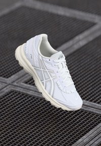 Weiße Sportschuhe aus synthetischem Material mit einem Mesh-Design, subtilen grauen Akzenten, abgerundeter Zehenpartie und gepolsterter Sohle.