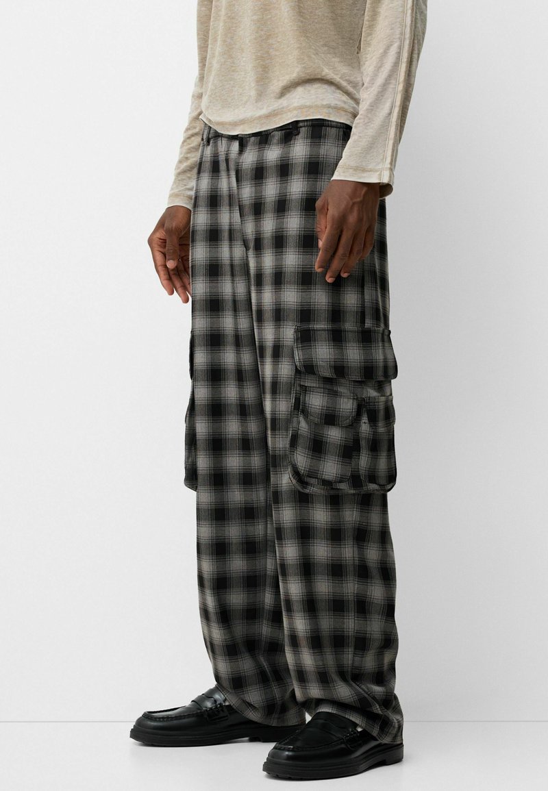 Pantalones cargo de cuadro en negro y gris con un corte holgado, que cuentan con dos bolsillos laterales y una tela texturizada. Combinados con zapatos negros.