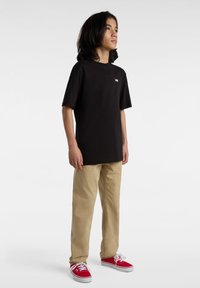 Musta lyhythihainen t-paita logolla, beige suorat housut ja punaiset tennarit valkoisilla nauhoilla. Sujuva kangas ja rento istuvuus.