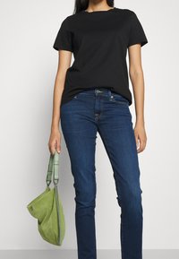Black cotton t-shirt with short sleeves, paired with blue denim jeans and a green suede bag with a structured shape and adjustable straps.