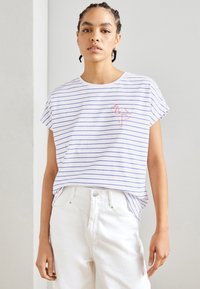 White cotton T-shirt with blue horizontal stripes, round neckline, short sleeves, and a red flamingo embroidery on the left side. Worn with white jeans.