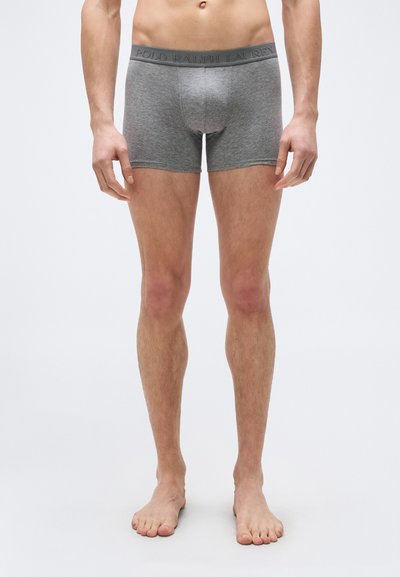 Άνδρας που στέκεται ξυπόλητος φορώντας γκρι εσώρουχα boxer της Polo Ralph Lauren σε απλό λευκό φόντο.