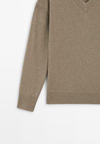 Beige V-Ausschnitt-Pullover aus weichem Strickmaterial, mit gerippten Bündchen und Saum, hat einen lässigen Schnitt und eine mittelschwere Textur.