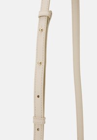 Béžový kožený popruh na tašku se zlatým kováním, s detailním prošíváním a nastavitelnými otvory pro přizpůsobení délky. Hladká textura.