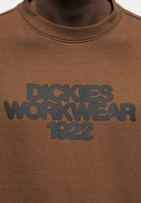 Sweatshirt marron à col rond avec un texte en relief noir indiquant "Dickies Workwear 1922" sur la poitrine.