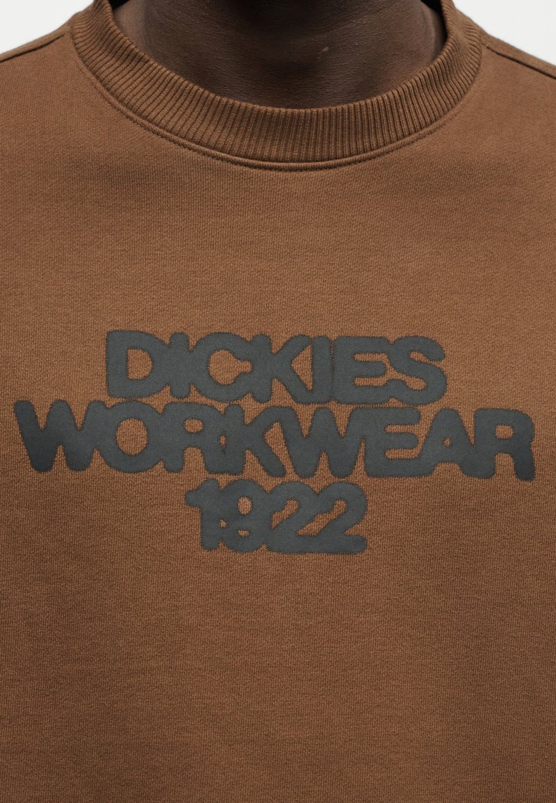 Brown crewneck sweatshirt with black raised text that reads "Dickies Workwear 1922" on the chest.