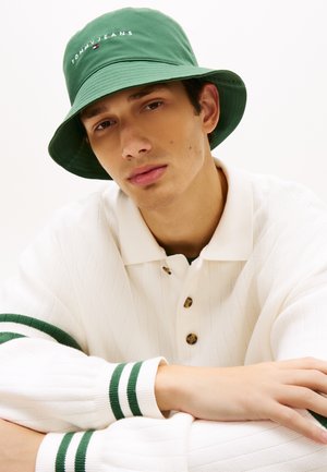 Πράσινο κάσκα με κεντημένο λογότυπο "TOMMY JEANS"· λευκό πλεκτό πουλόβερ με πράσινες ρίγες στις μανσέτες· λεπτομέρειες με κουμπιά στο γιακά.