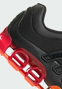 Crna atletska cipela s teksturiranim mrežastim gornjim dijelom, elegantnim dizajnom i živopisnim crvenim akcentima na obloženom potplatu s istaknutim zračnim džepovima.