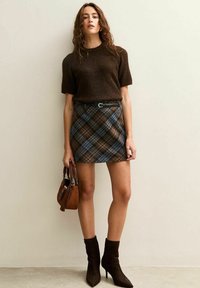 Un pull en tricot marron à manches courtes associé à une mini-jupe à carreaux marron et bleu. Comprend une ceinture noire et un sac à main marron. Bottines marron.