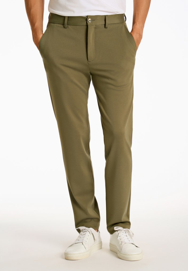 Olijfgroene broek van een zachte stof, met een knoopsluiting, zijzakken en een slim fit. Gecombineerd met witte sneakers.