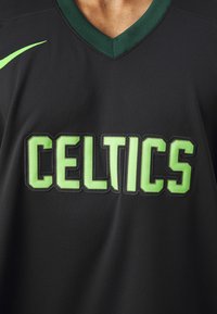 Čierny atletický dres s zeleným nápisom "CELTICS", s véčkovým výstrihom a texturovanou tkaninou. Logo Nike v zelenej farbe na ramene.