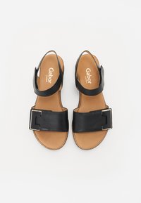 Black leather sandals with a wide strap, gold buckle accent, and adjustable ankle strap; tan footbed and textured sole for grip.