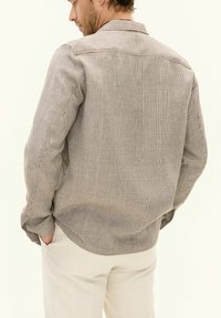 Button-up shirt with a brown and beige checkered pattern, long sleeves, a collar, and a loose fit, made from lightweight fabric.