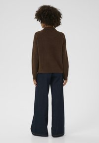 Brown knitted sweater with a high neck, paired with wide-leg dark blue denim pants. The fabric appears soft with a smooth texture.