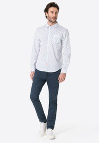 White button-up shirt with blue floral pattern; long sleeves, chest pocket; paired with navy pants and white sneakers.