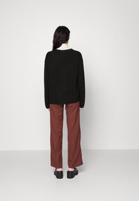Suéter negro de gran tamaño con dobladillo acanalado, combinado con pantalones anchos marrones y zapatos negros gruesos. Diseño simple y minimalista.