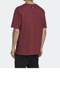 Bordeauxfarvet bomulds T-shirt med korte ærmer og rund halsudskæring, med et sort logo mærke på ryggen, vist fra en bagvinkel.